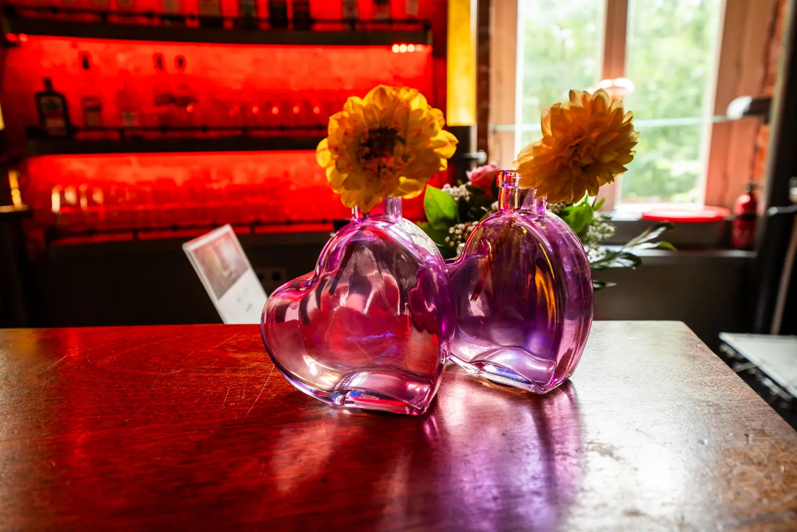 Blumen in rosa Vasen auf dem Bartresen vor beleuchtetem Regal, Sander Dickkopp in Hamburg-Lohbr&uuml;gge
