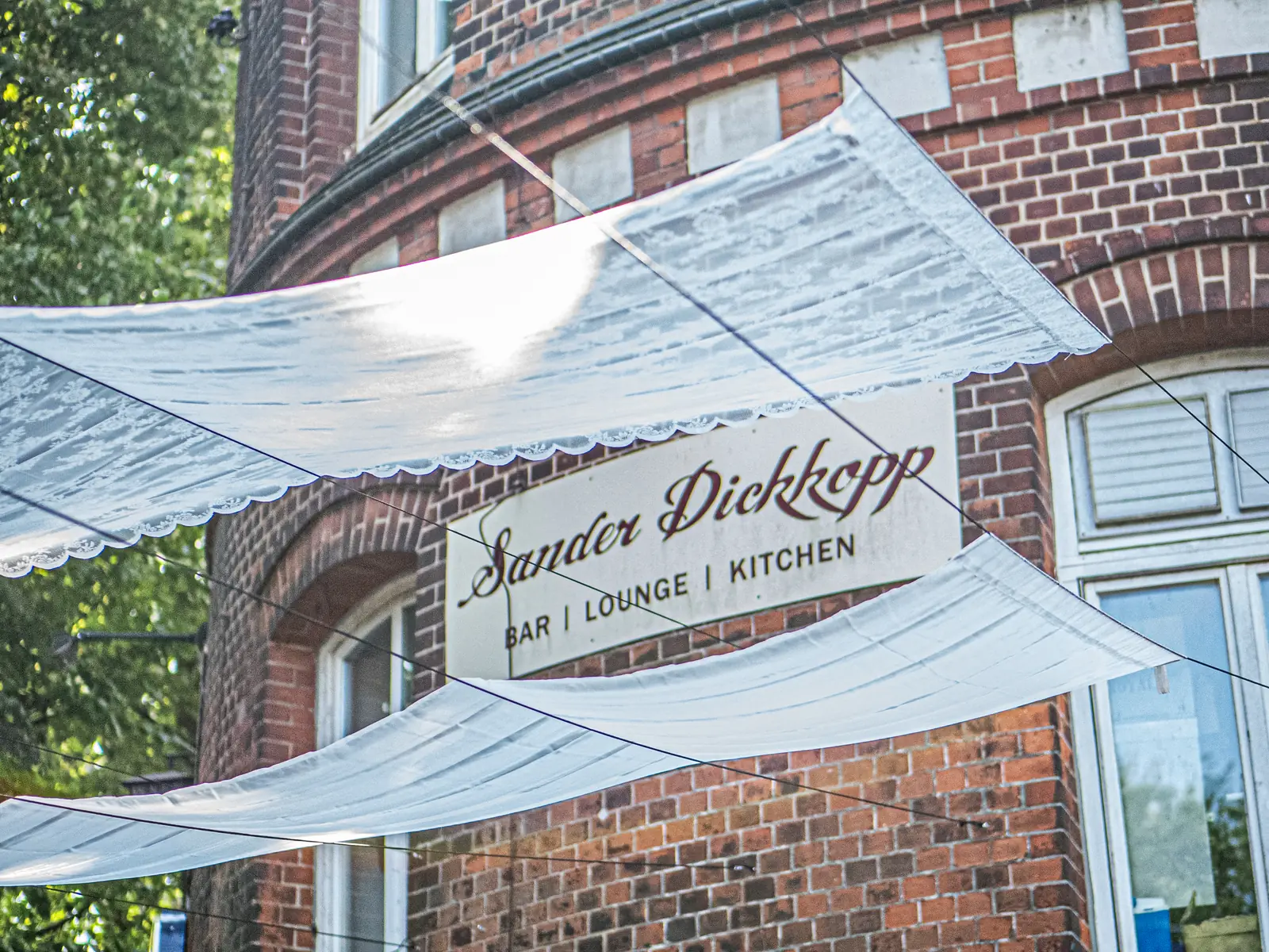 Backsteinfassade mit Schild Sander Dickkopp Bar Lounge Kitchen und weißen Sonnensegeln, Hamburg-Lohbrügge