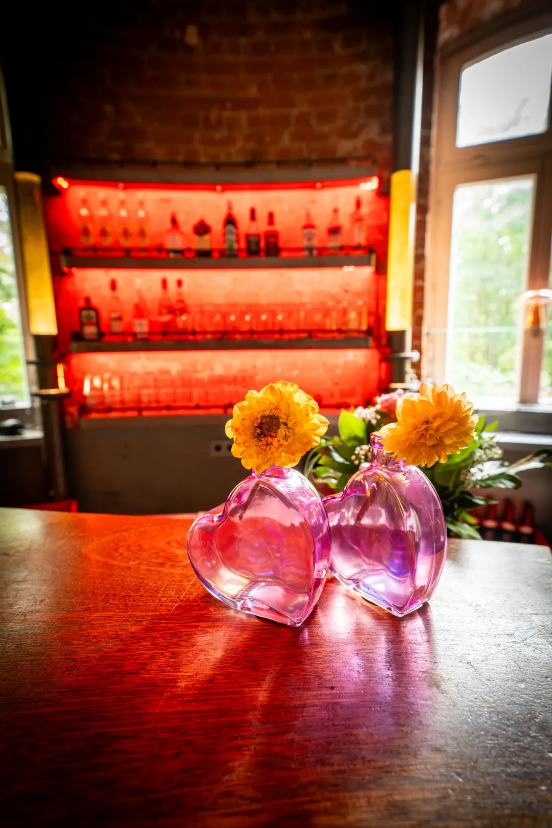 Blumen in rosa Vasen auf dem Tresen vor beleuchtetem Flaschenregal, Sander Dickkopp in Hamburg-Lohbr&uuml;gge