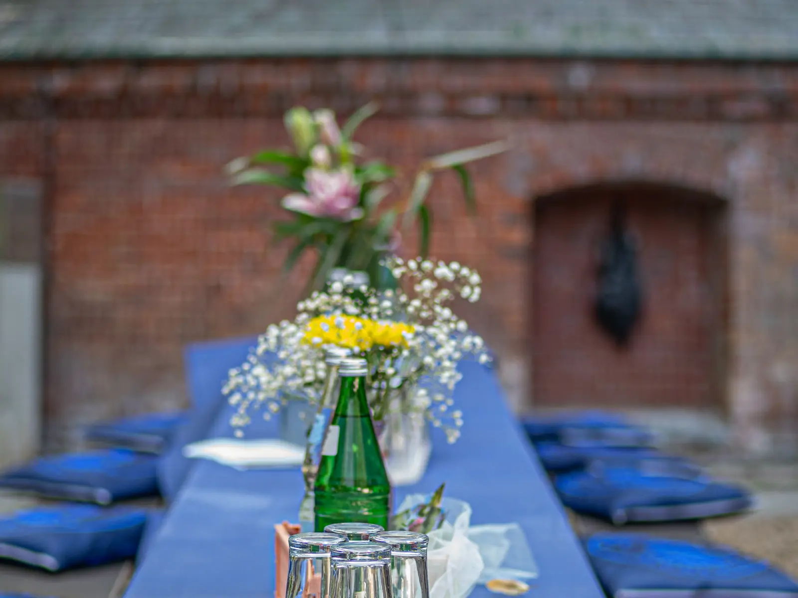 Lange gedeckte Tafel mit blauer Decke und Blumen vor der Backsteinfassade, Außenbereich Sander Dickkopp